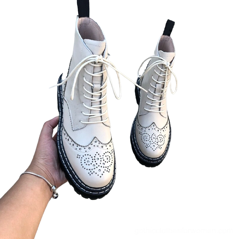 Pair of off-white leather gothic brogue boots in hand with cream laces visible, displaying brogue perforations and black sole