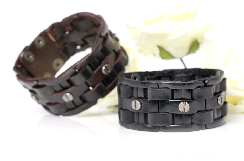 Pair of hand-woven leather gothic bracelets with metal accents, side angle view with white floral decoration, displaying woven texture and craftsmanship