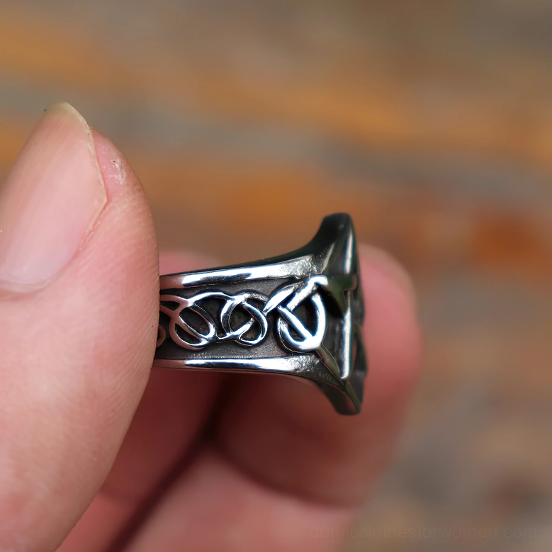 Pentagram ring side close-up held by human finger, displaying dark polished stainless steel and Celtic knotwork details