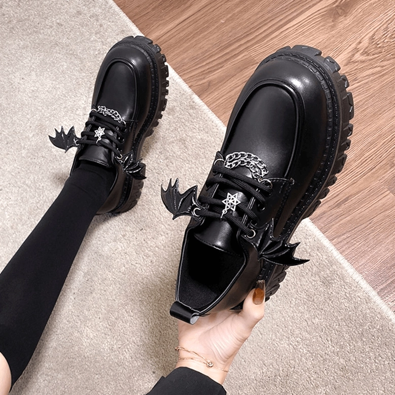 Female model wearing black platform loafers with bat wing details and gothic hardware, styled with black socks, overhead angled view
