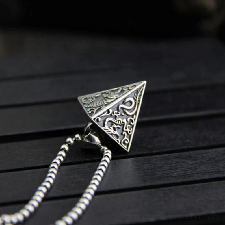 Vintage sterling silver pyramid pendant with clear dragon-themed carvings on beaded chain, oblique top view on dark slatted wood desktop