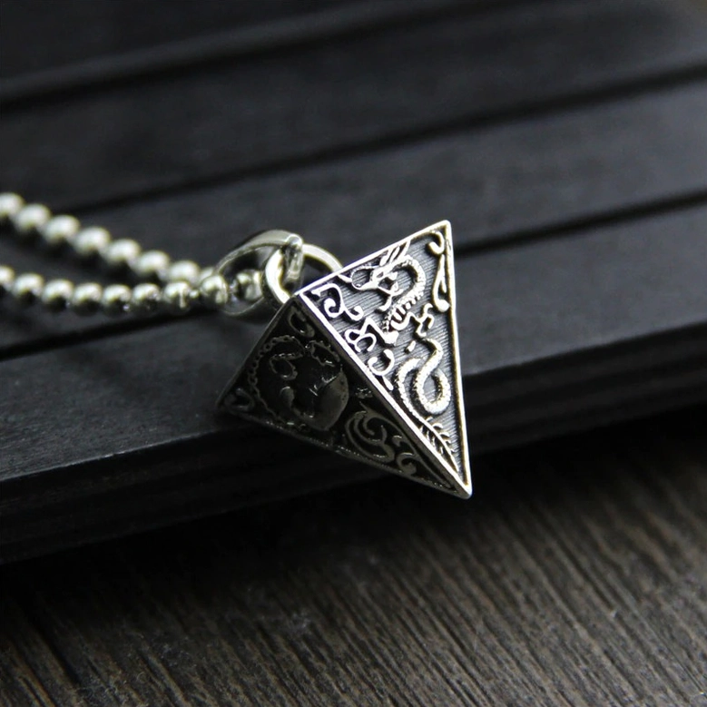 Pyramid pendant on beaded chain with dragon and floral engravings, low side view on dark wood grain surface displaying gothic pendant chain styling