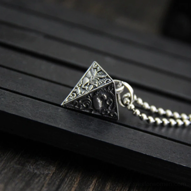 Antique 925 silver pyramid pendant with mixed embossed animal patterns, side oblique view on dark slatted wood table showcasing vintage gothic jewelry