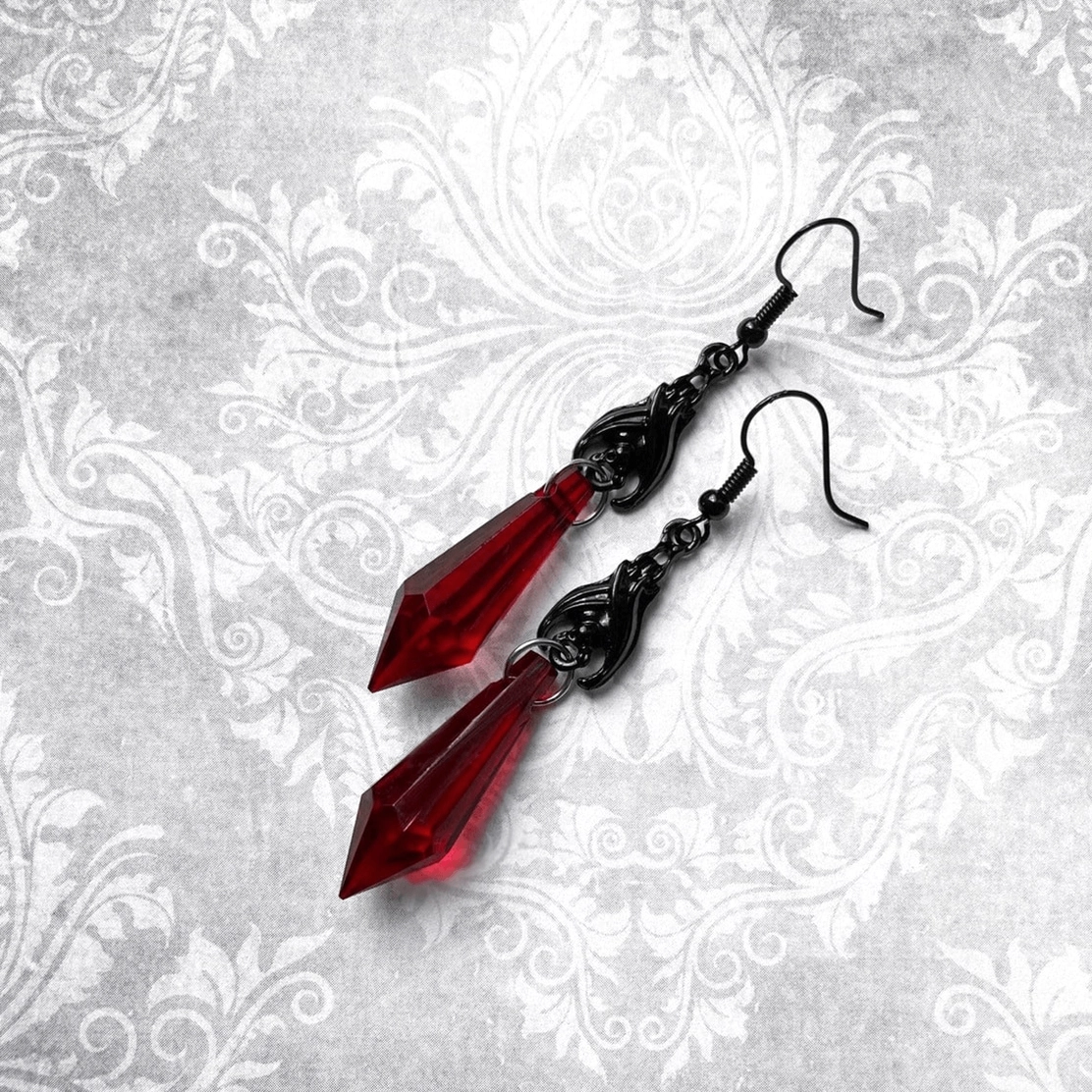 Alternative gothic bat earrings with red transparent spikes displayed on vintage damask fabric, alternative jewelry styling