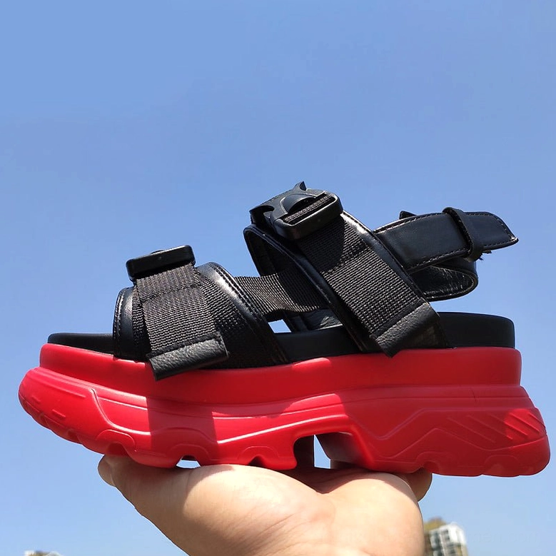 Red and black platform sandals worn with hand, outdoor view showing thick lugged outsole