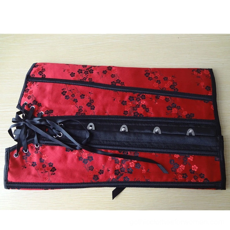 Red floral gothic corset back flat lay showing black lace-up closure with multiple metal eyelets and red floral fabric pattern on wooden background