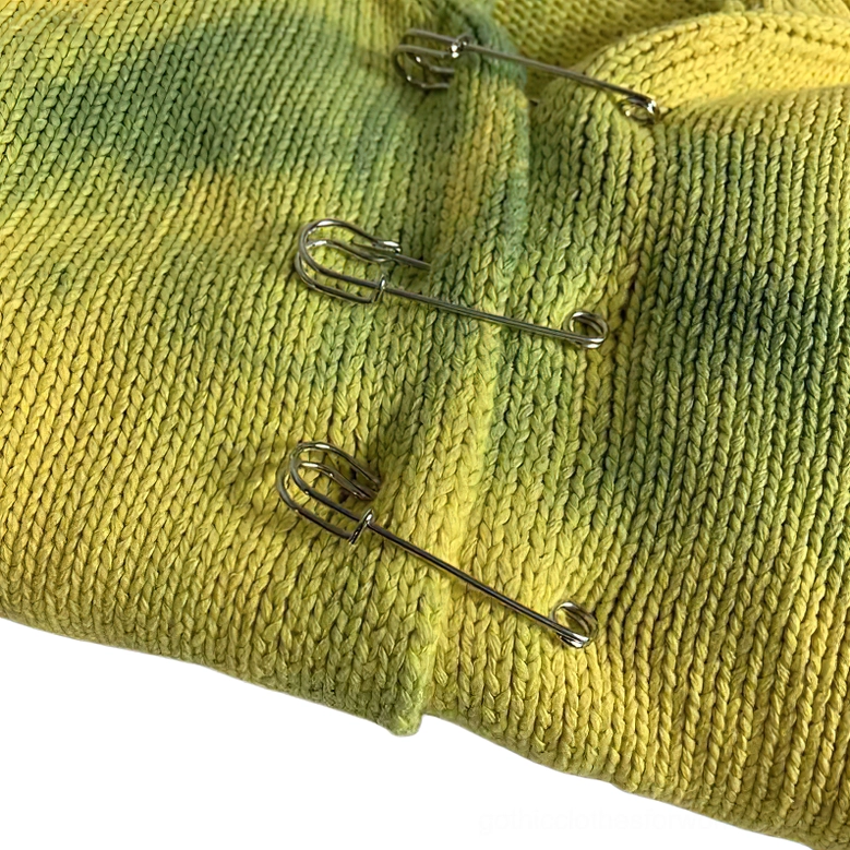 Close-up detail of silver safety pin fasteners on knitted tie-dye cardigan fabric