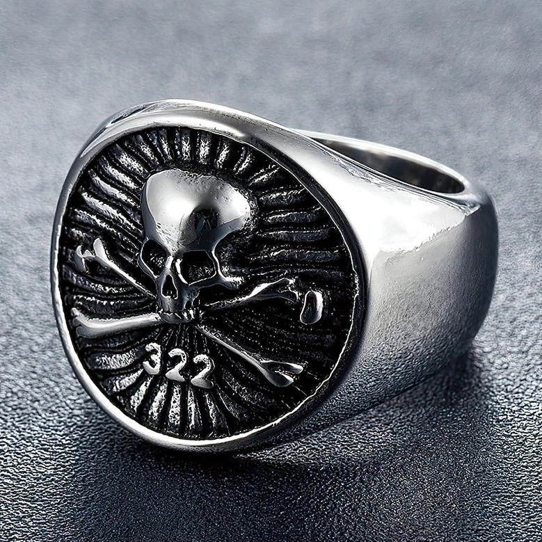 Silver skull signet ring with crossbones on dark leather background, showing radial texture detail
