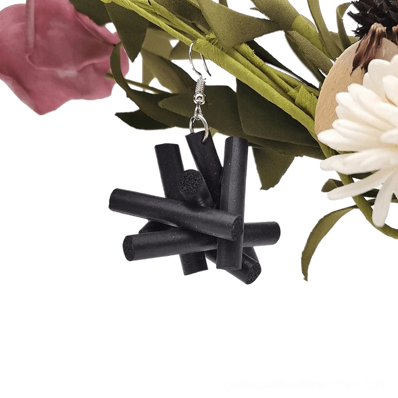 Single black rubber drop earring with crossed-stick structure and silver metal hook clasp on floral background