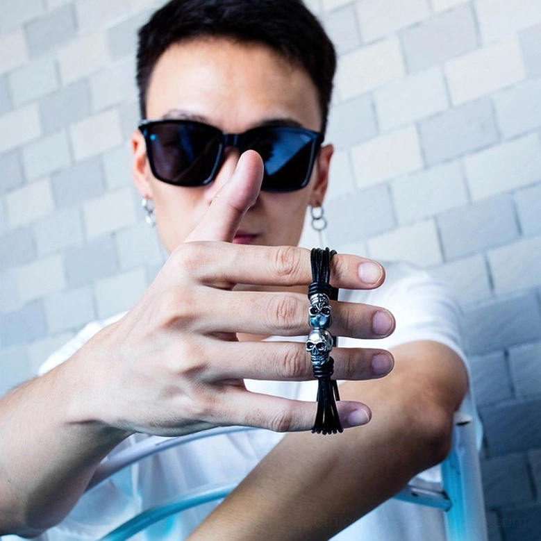 Male model wearing dual skull bracelet holding product close-up with tassel detail on mosaic tile background