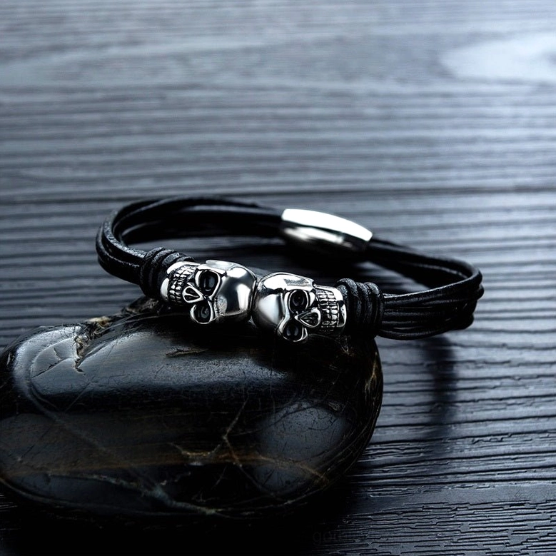 Stainless steel dual skull leather bracelet detail shot on dark polished stone surface
