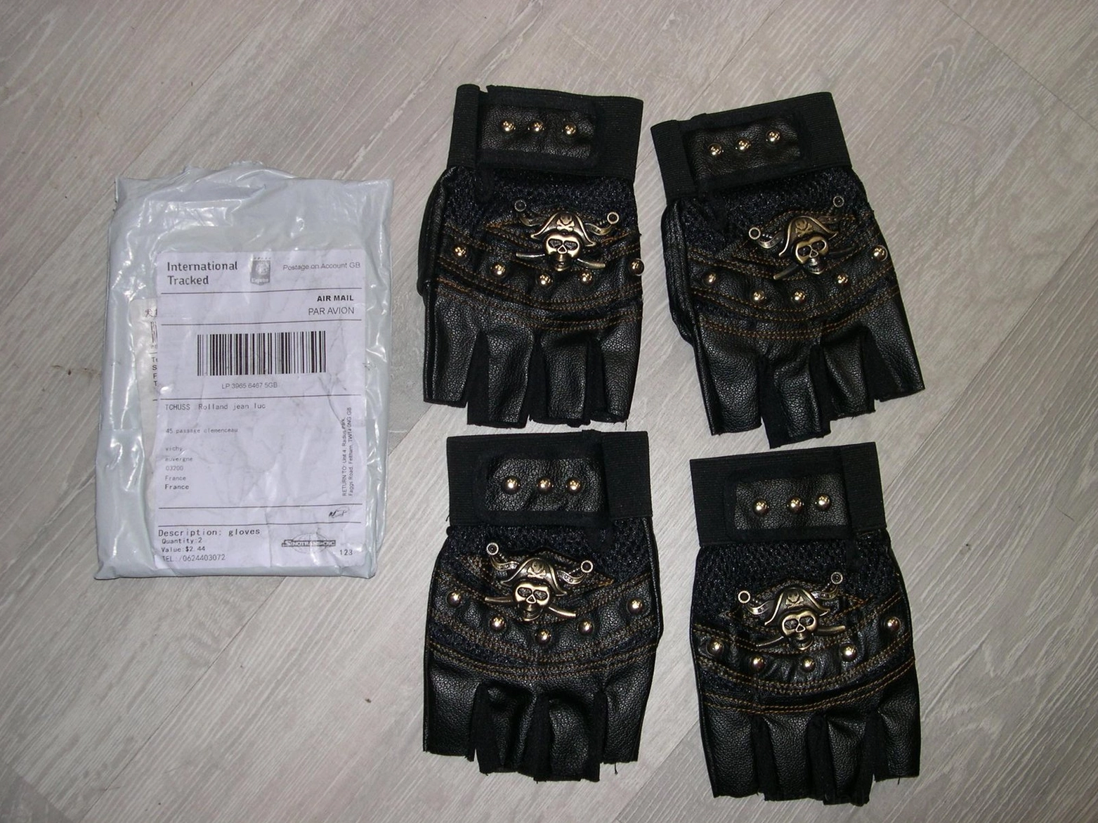 Multiple skull rivet fingerless gloves pairs stacked on wooden surface with shipping parcel showing product collection