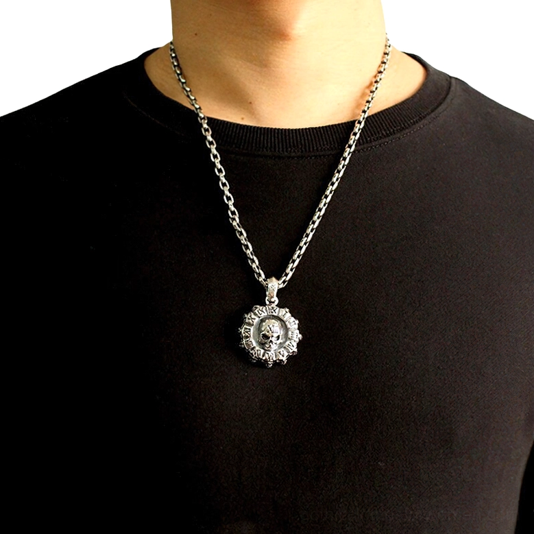 Male model wearing gothic skull pendant necklace on silver curb chain, displayed at chest level against black shirt, demonstrating wearable styling and appropriate pendant positioning