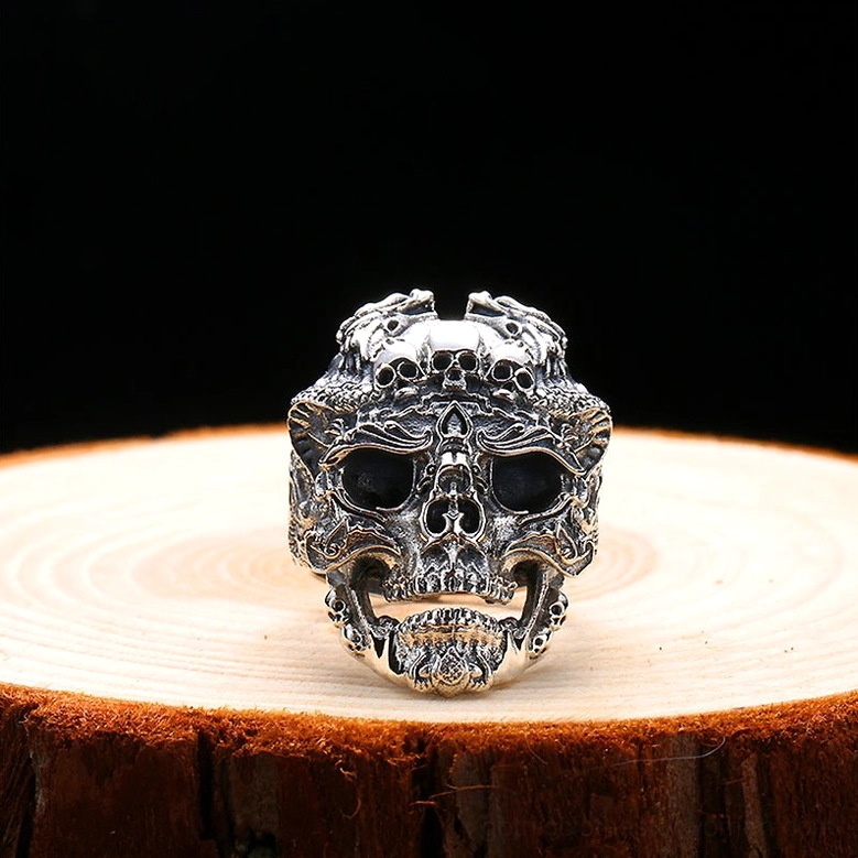 Open-jaw skull ring front view with detailed facial engravings and antiqued silver finish on wooden display