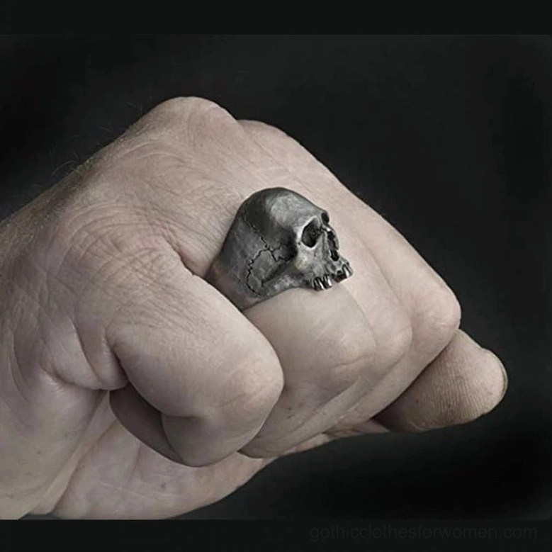 Silver skull ring worn on index finger, side fist view against black background