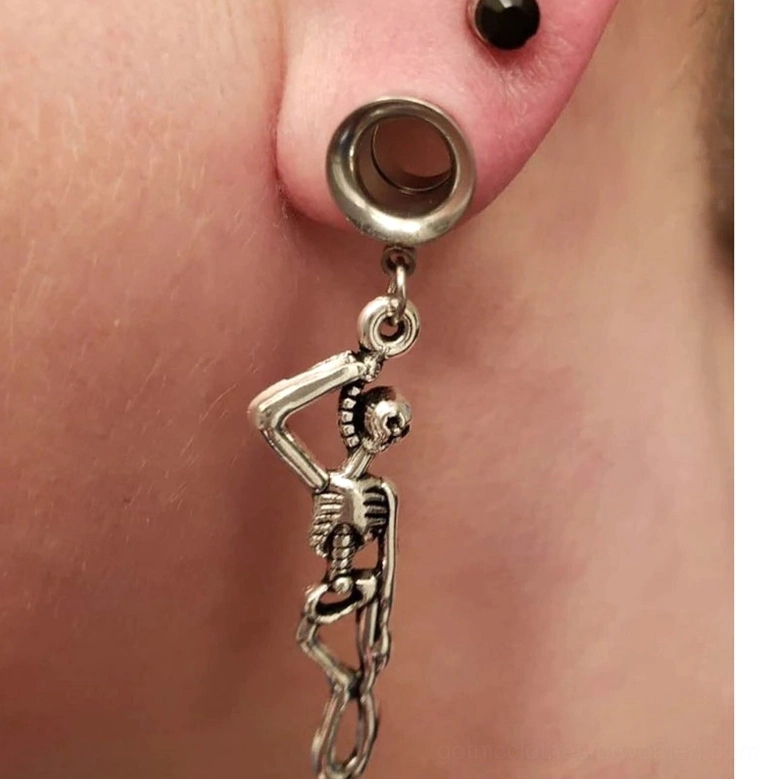 Antique dark silver skull ear tunnel on earlobe – memento mori dangle earring showing patina finish and worn aesthetic