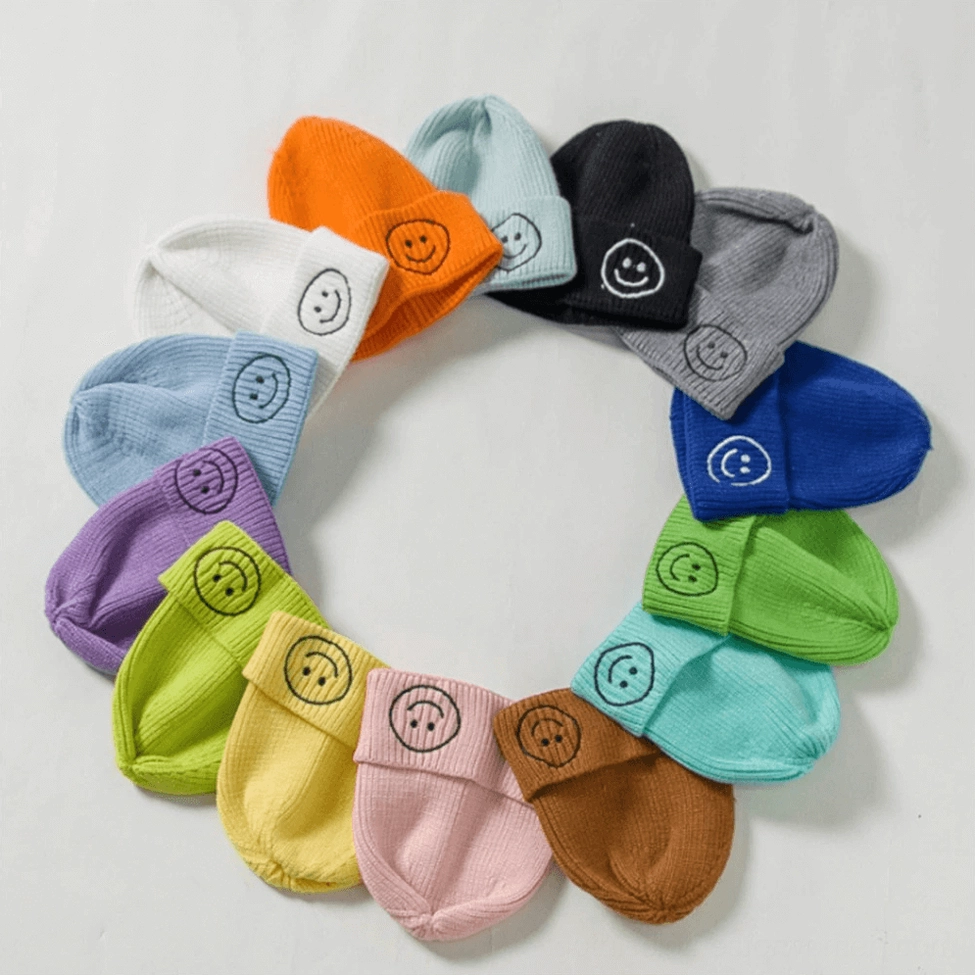 Multiple color options of smiley face embroidered knit beanies arranged, dark aesthetic winter hat color selection