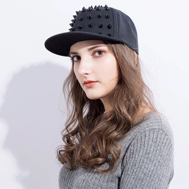 Female model wearing black spiked snapback cap with metal cone decorations, front portrait
