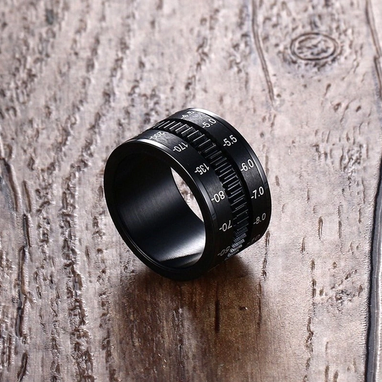 Alternative jewelry camera lens spinner ring three-quarter view with detailed parameter markings on wood background