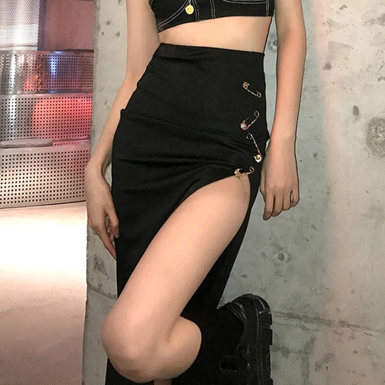 Black split midi skirt with safety pins styled on model with cropped top against industrial concrete background, showing high side slit