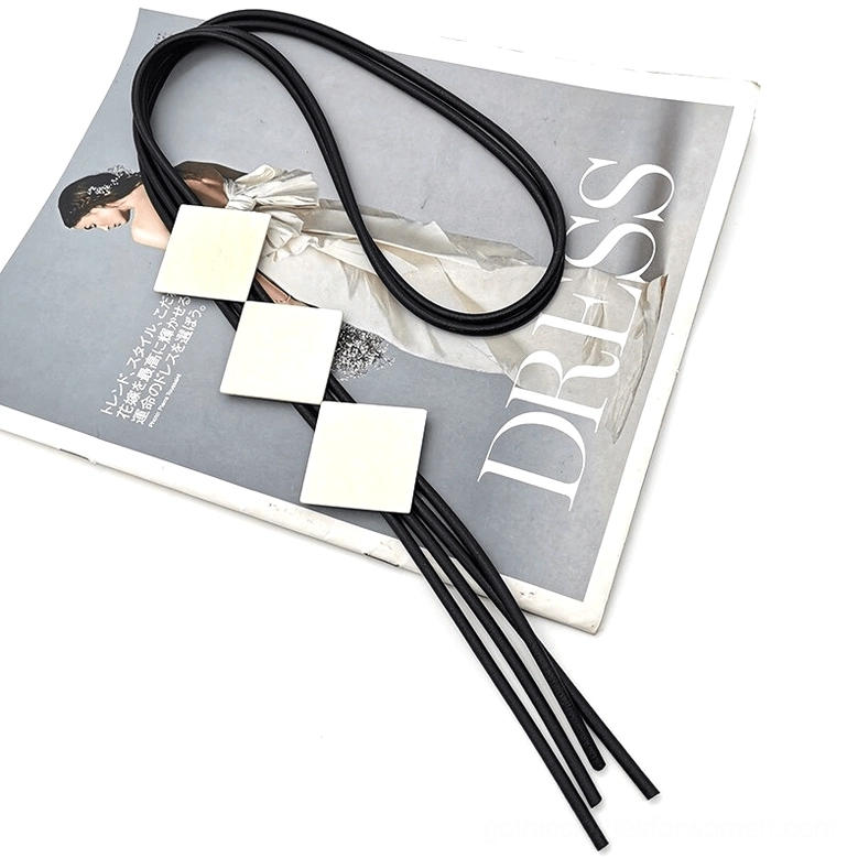 Wooden pendant lariat necklace flat lay displayed on vintage fashion magazine surface, showing three square wood beads with black rubber tassel cord