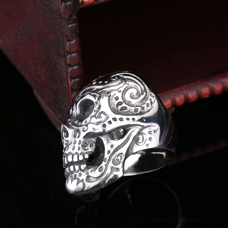 Polished silver stainless steel biker skull ring displayed on dark wooden jewelry box, low side profile showcasing engraved design depth