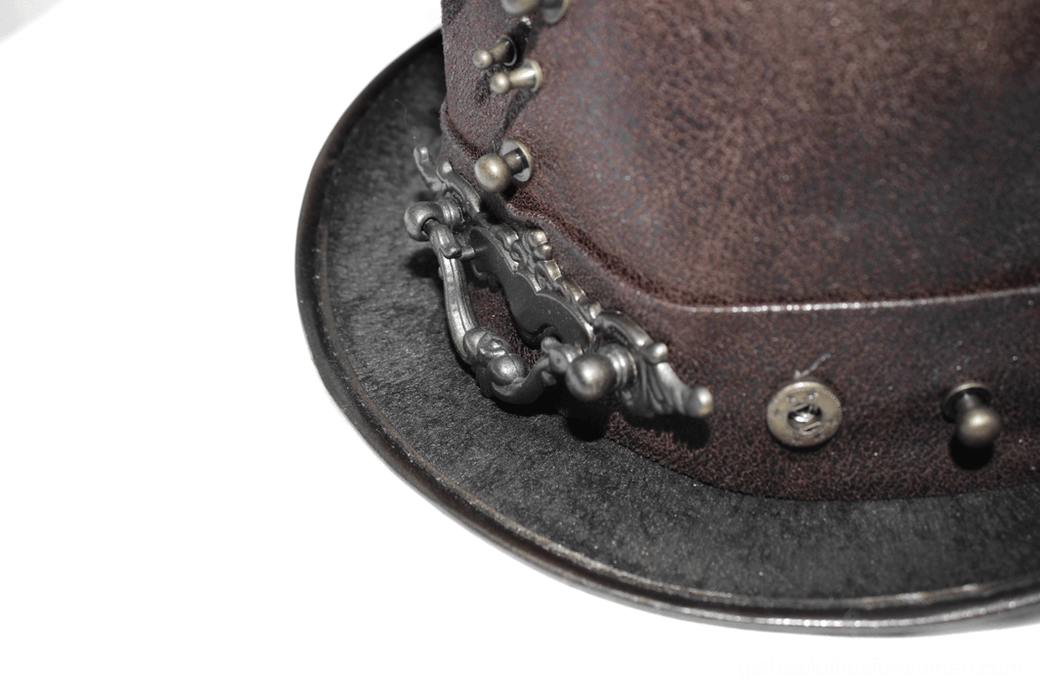 Detailed view of steampunk hat metalwork showing bronze rivets, skull ornament, and decorative hardware on dark brown leather surface