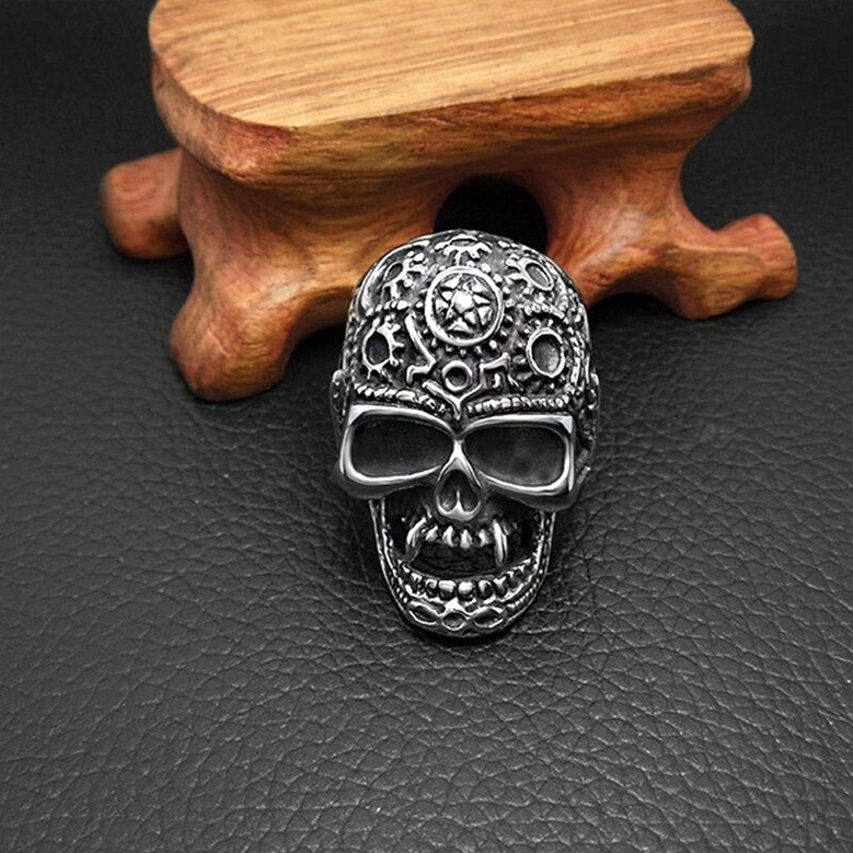 Detailed front view of steampunk skull ring with intricate gear engraving on dark silver tone stainless steel, displayed on leather mat
