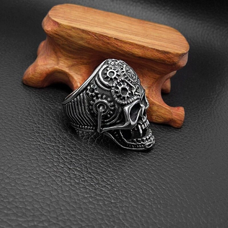 Gothic skull gear ring shown from right side angle on leather and wood display, highlighting vintage steel engraved band texture