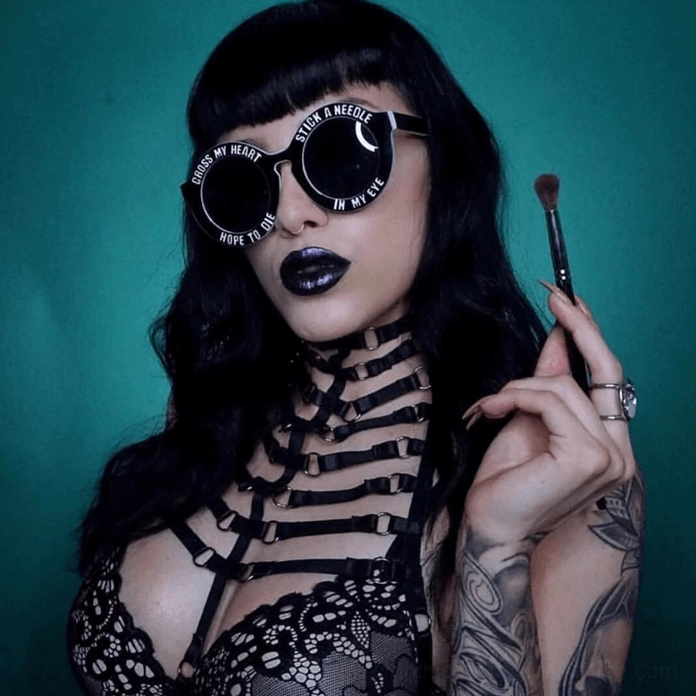 Gothic strappy harness bra worn by tattooed model, matching dark goth styling, upper body close-up