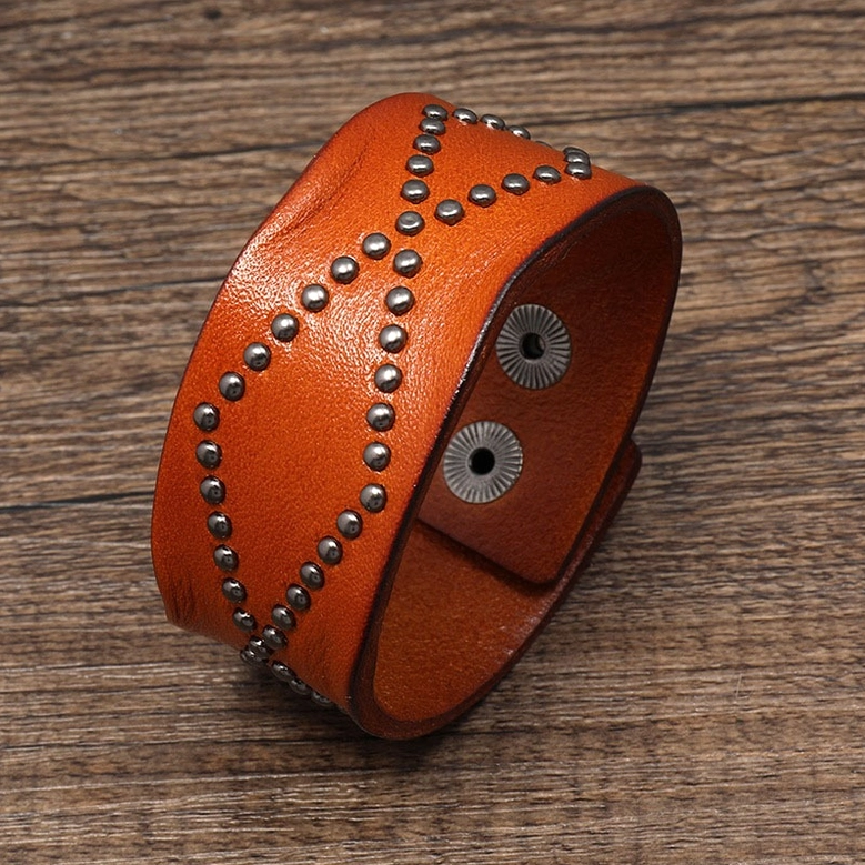 Tan-brown leather gothic cuff bracelet with cross pattern rivets and snap closure, side profile view on wooden background
