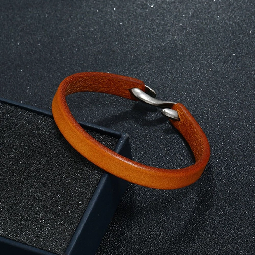 Light brown leather narrow cuff bangle with vintage clasp next to black gift box on dark background
