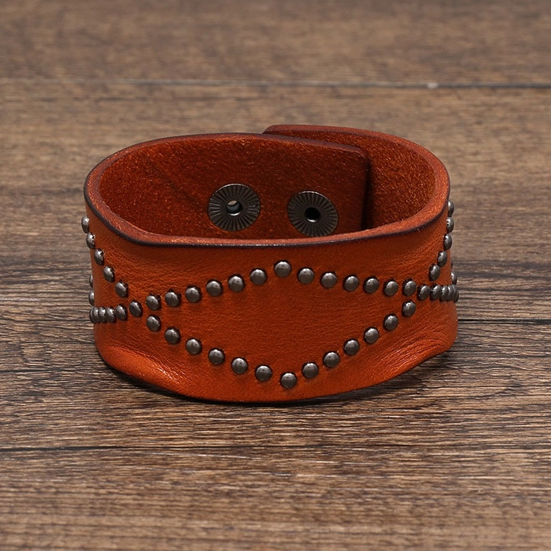 Tan leather gothic cuff bracelet featuring round rivet trim and industrial snap fastener, top-down flat lay on wooden table