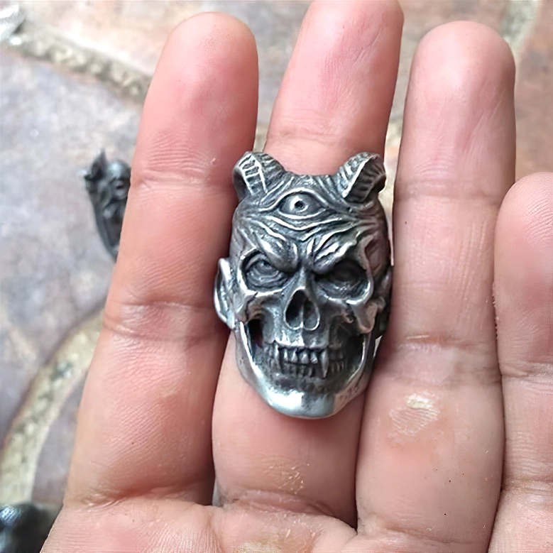 Front palm view of three-eyed demon skull ring showing aged silver finish with sharp fangs and twin horns