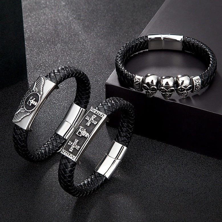 Three gothic punk leather bracelets arranged on dark surface - cross emblem, winged skull, and triple skull designs showcase