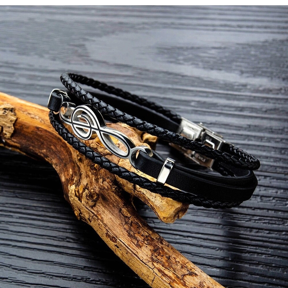 Treble clef leather bracelet side top-down view on driftwood background showing braided texture and silver metal accents