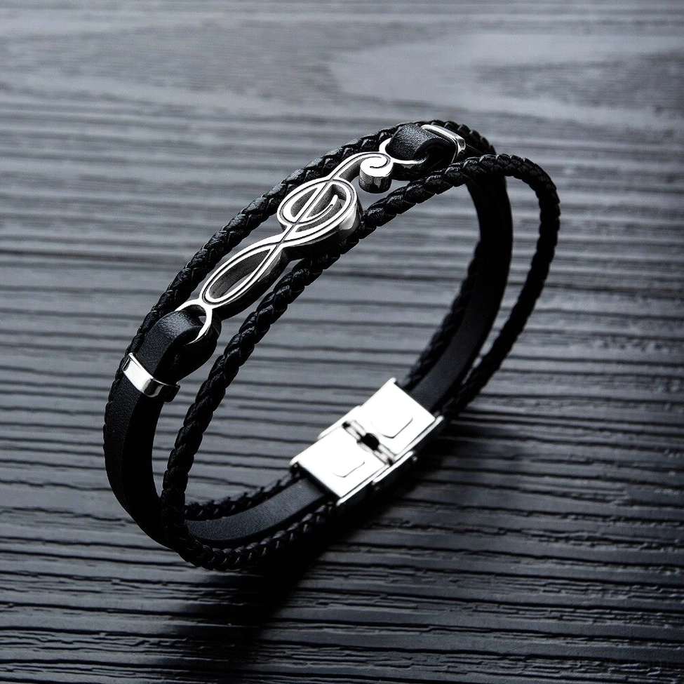 Close-up front view of black PU leather treble clef bracelet with stainless steel buckle on dark wood tabletop