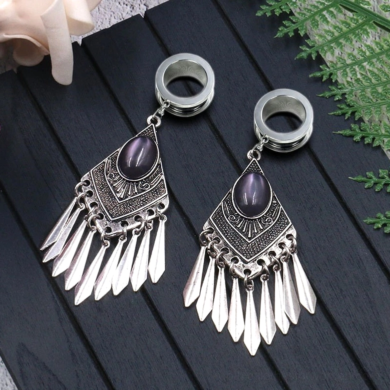 Tribal gothic tunnel earrings pair on dark wooden surface with fern decoration - atmospheric gothic jewelry display