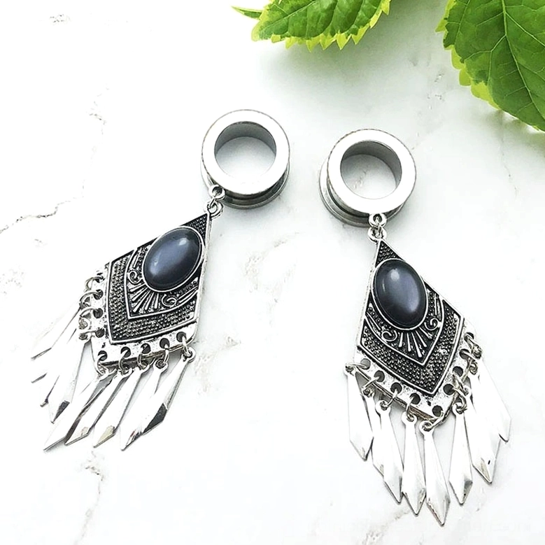 Tribal gothic tunnel earrings on white marble with green leaves - luxe alternative jewelry presentation