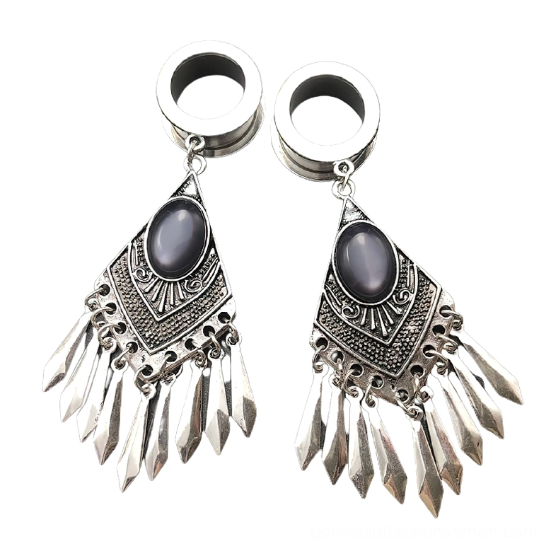 Tribal gothic tunnel earrings pair - silver surgical steel with dark oval gemstones and carved tribal patterns with spike tassel pendants, flat lay overhead view