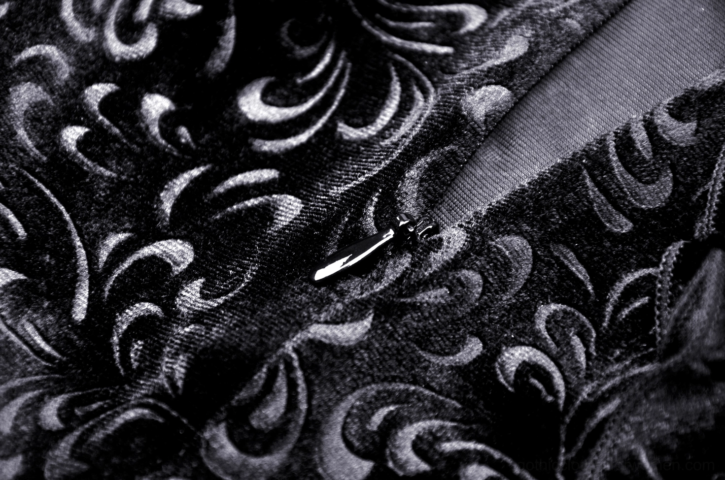 Swirling black velvet fabric texture with metal fastener and satin trim detail close-up