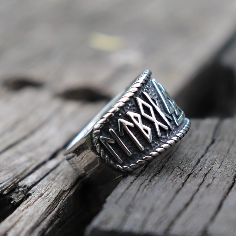 Viking rune amulet ring with Valknut and rune engravings on antique silver stainless steel, oblique front angle on weathered wood background