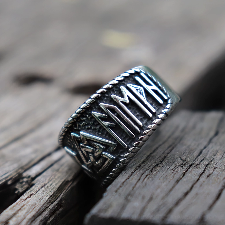 Stainless steel Viking rune ring oblique side close-up showing detailed rune engravings, twisted rope trim, and antique silver tone on weathered wood