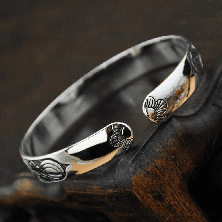 Adjustable open cuff bracelet low angle view showing carved floral engraved open ends and polished silver metal construction