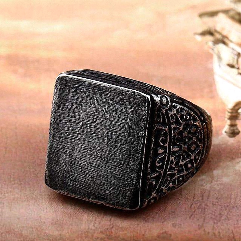 Distressed dark stainless steel gothic square ring with aged patina finish displayed on warm wooden surface