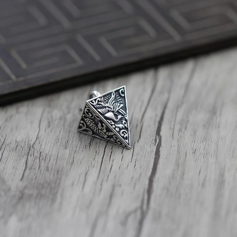 Vintage sterling silver pyramid pendant with delicate facet engravings, top oblique view on light wood grain desktop highlighting gothic jewelry details