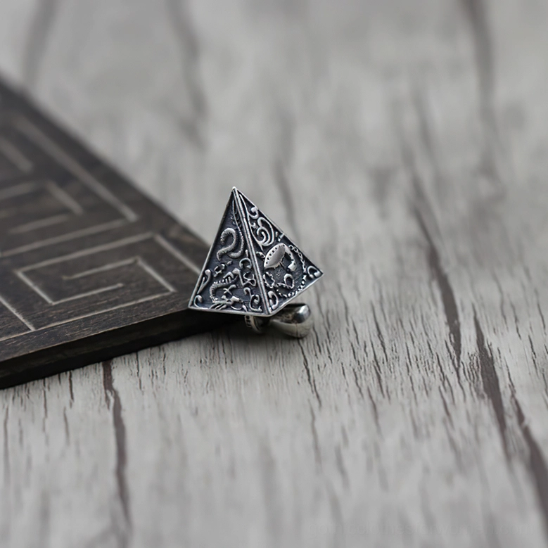 Antique sterling silver pyramid pendant with intricate engraved patterns, side oblique view on light wood desk with geometric decor background