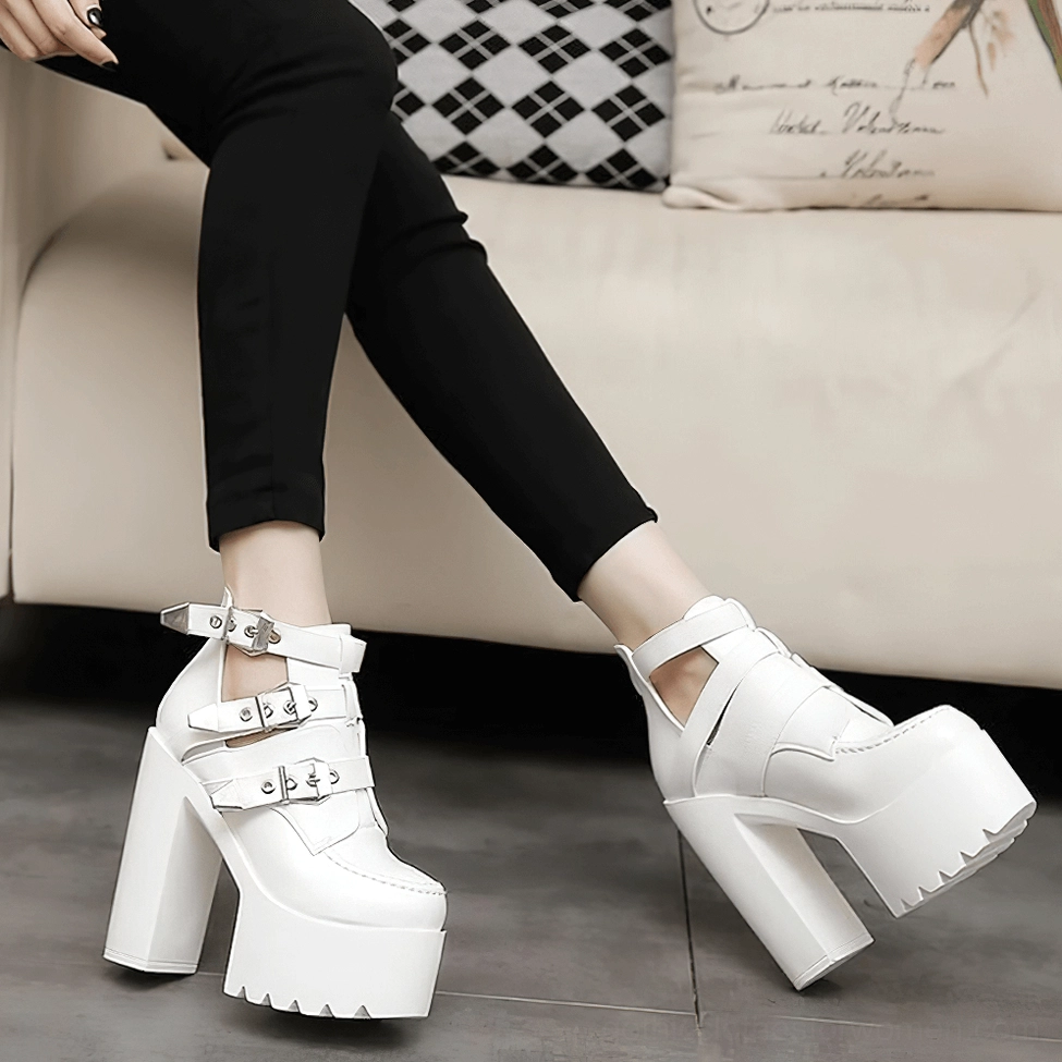 White gothic platform ankle boots worn with skinny black pants - low-angle leg view showing solid smooth leather finish and dramatic platform heel