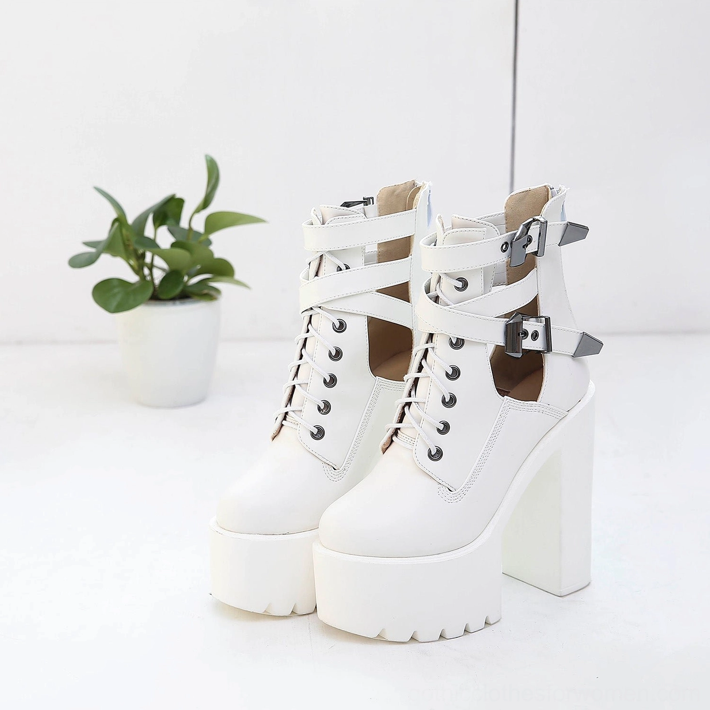 White gothic platform lace-up ankle boots with decorative metal buckle straps, cutout side panels, and commanding round toe design in lifestyle setting
